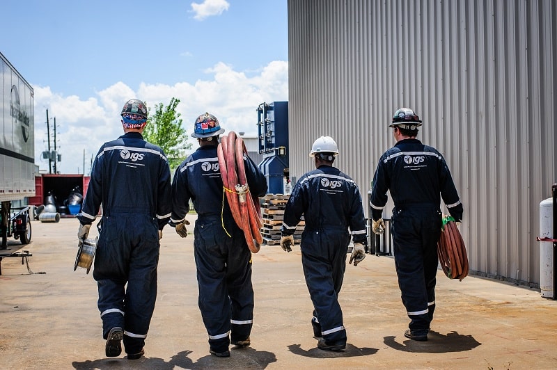 Four men in overalls carrying industrial equipment